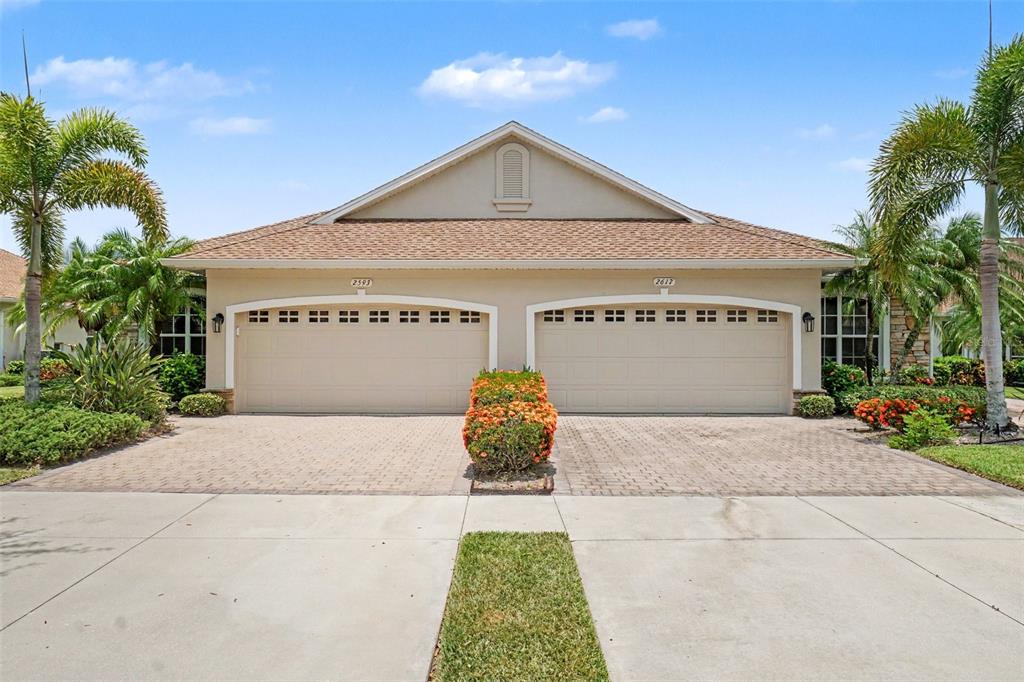 A duplex home features two garage doors, a paved driveway, and palm trees under a sky — 2593 COTTONWOOD LANE, NORTH PORT, FL