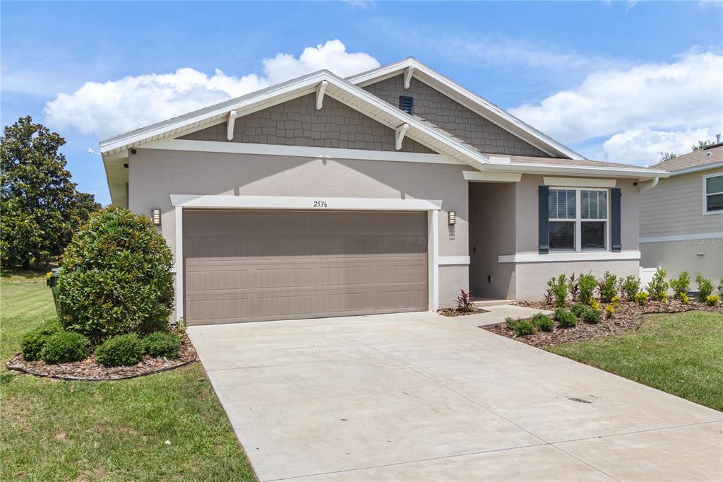 A single-story suburban house with a beige stucco exterior, brown garage door, and shingled roof — 2536 AUTUMN STREAM DRIVE, LEESBURG, FL