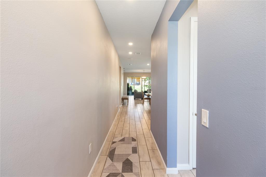 A hallway with light-colored tile flooring leads toward an open living area with sliding doors — 2536 AUTUMN STREAM DRIVE, LEESBURG, FL