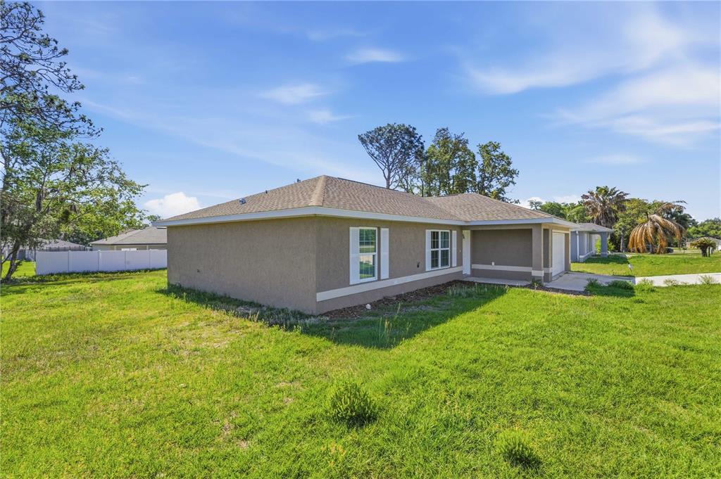 A side view of a single-story tan house with a hip roof and grass yard — 407 MARION OAKS COURSE, OCALA, FL