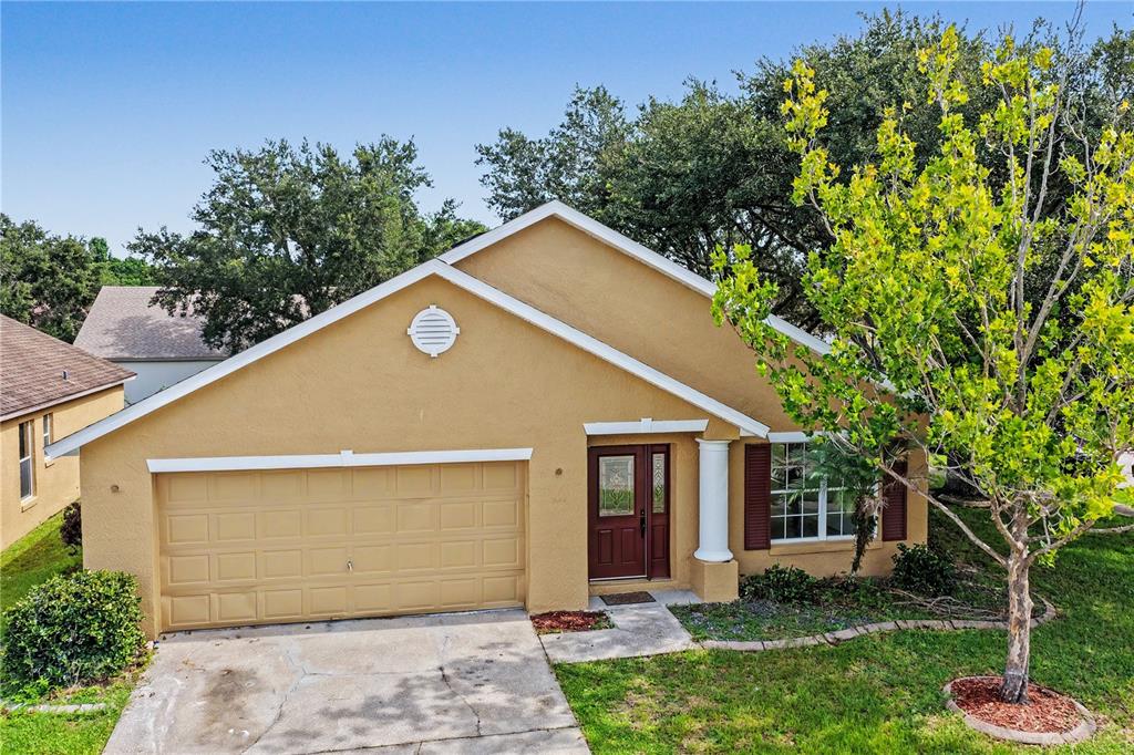 A tan, single-story house with a two-car garage, a red front door, and a tree — 544 CYPRESS TREE COURT, ORLANDO, FL