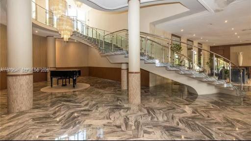 A grand foyer features a curved staircase, marble flooring, and a black grand piano — 5401 Collins Ave # 526, Miami Beach FL 33140, MIAMI BEACH, FL