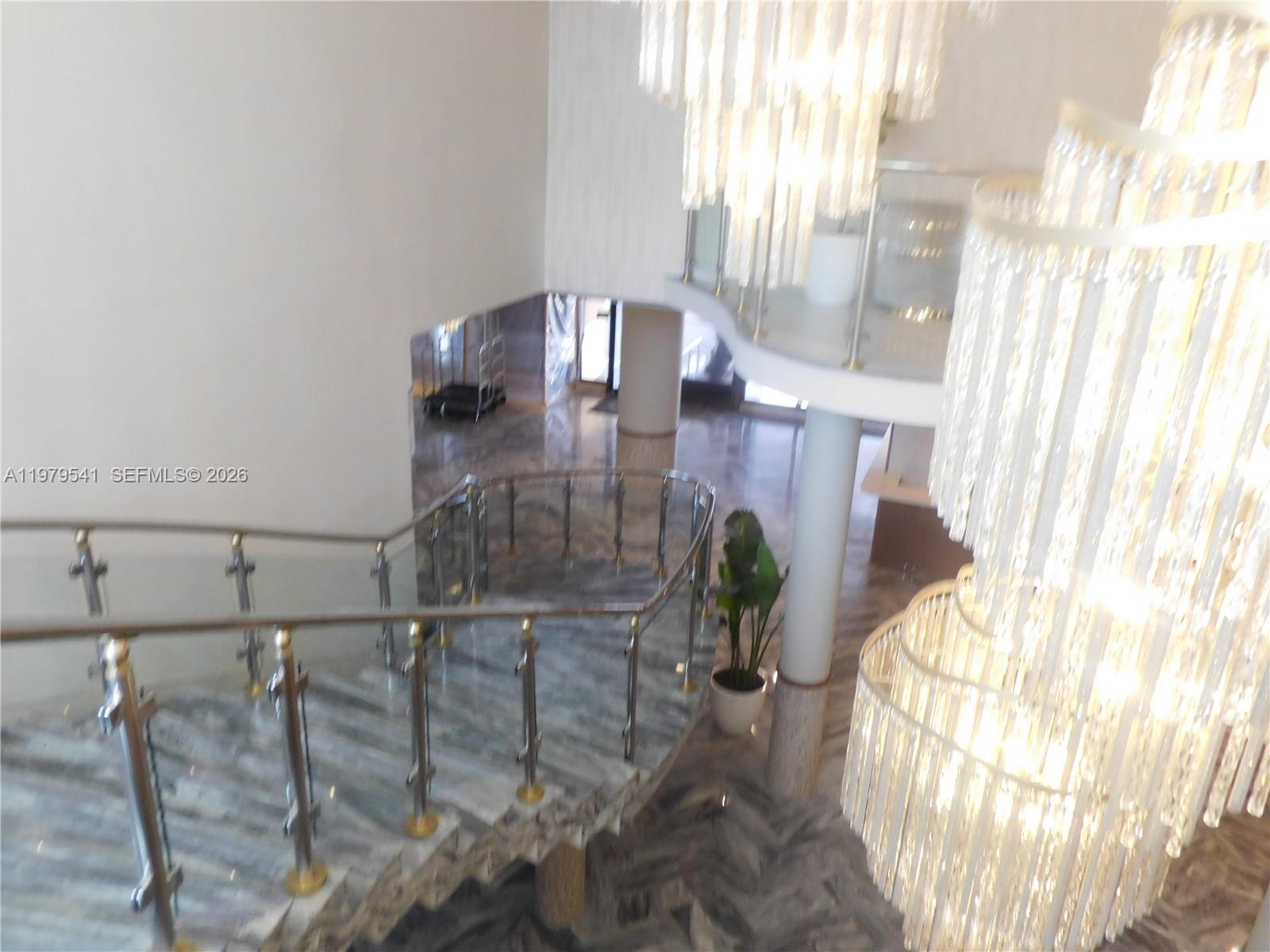 A curved marble staircase features a glass railing and a large crystal chandelier overhead — 5401 Collins Ave # 526, Miami Beach FL 33140, MIAMI BEACH, FL