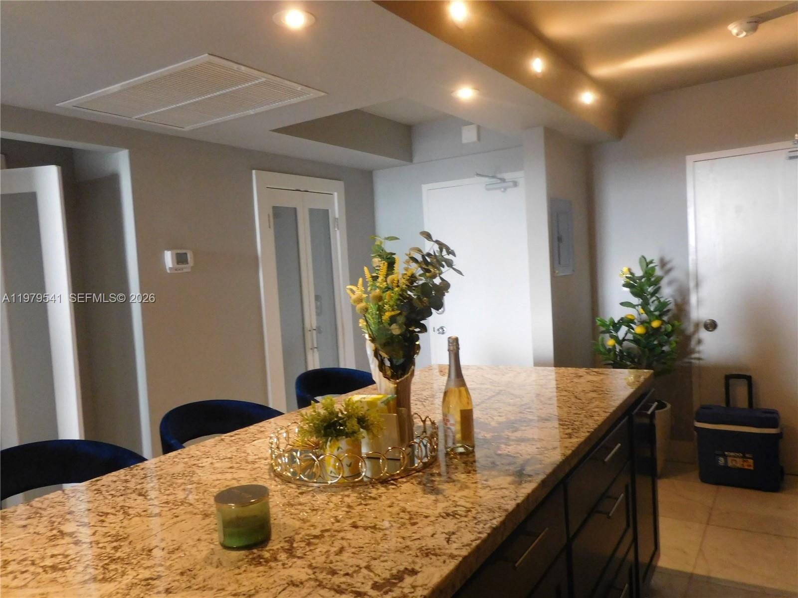 A kitchen island with granite countertops sits in front of blue chairs and doors — 5401 Collins Ave # 526, Miami Beach FL 33140, MIAMI BEACH, FL