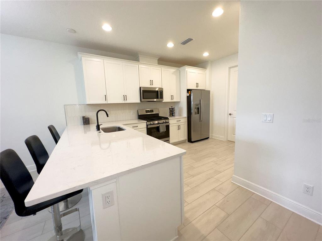 A modern kitchen features white cabinetry, stainless steel appliances, and a large quartz-topped island — 17881 CHERISHED LOOP, BRADENTON, FL
