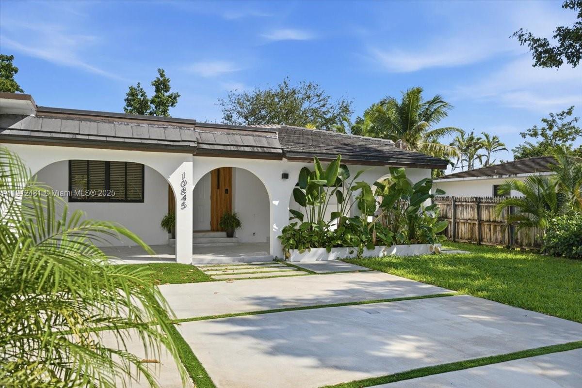 A white single-story house features an arched entryway and a concrete driveway with grass strips — 10845 Peachtree Dr, Miami FL 33161, MIAMI, FL