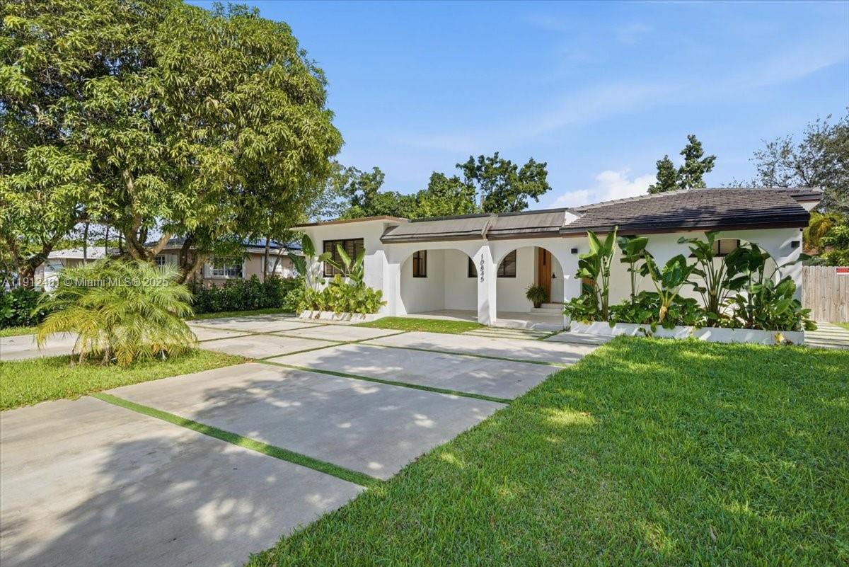 A white single-story house features a covered entryway with arched openings and a concrete driveway — 10845 Peachtree Dr, Miami FL 33161, MIAMI, FL