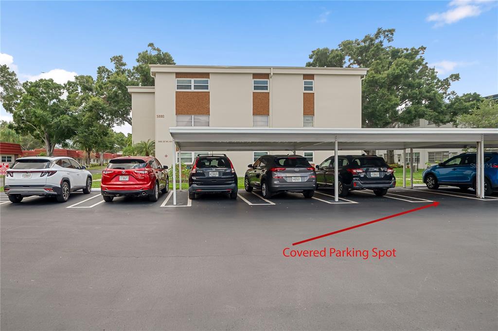 A multi-story apartment building exterior with a row of covered parking spaces in front — 5880 38TH AVENUE N UNIT 109, ST PETERSBURG, FL