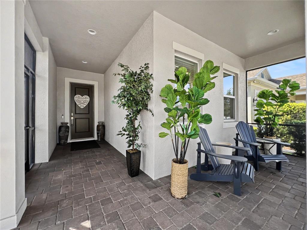 A covered patio features dark paver flooring, two Adirondack chairs, and several potted artificial plants — 2159 LIMESTONE TRAIL, KISSIMMEE, FL