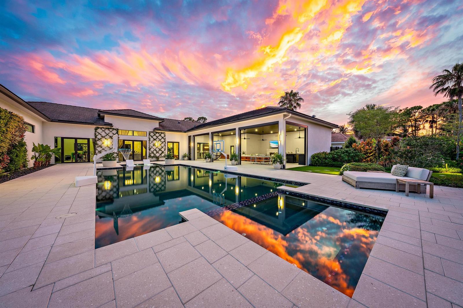 A modern house exterior features a swimming pool, spa, and covered patio at sunset — 6634 Audubon Trace W, West Palm Beach FL 33412, WEST PALM BEACH, FL