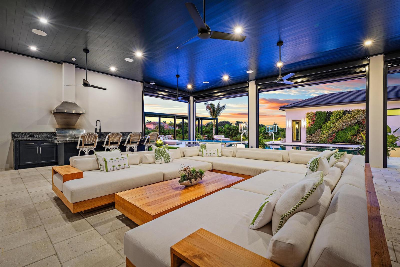 A modern outdoor living space features a large sectional sofa, kitchen area, and pool view — 6634 Audubon Trace W, West Palm Beach FL 33412, WEST PALM BEACH, FL
