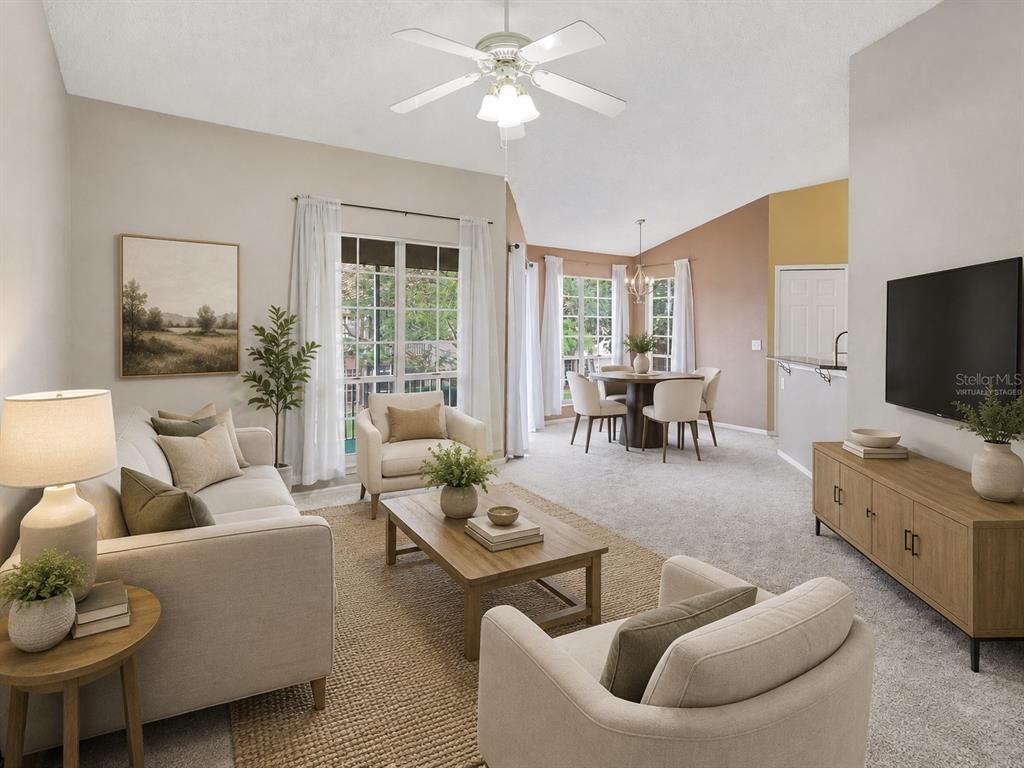 A living room and dining area with vaulted ceilings, carpeted floors, and neutral furniture — 4696 SUSSEX TERRACE UNIT 202, ORLANDO, FL