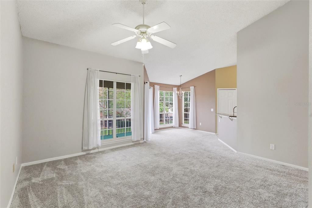 A living room with gray carpet, a vaulted ceiling, a ceiling fan, and large windows — 4696 SUSSEX TERRACE UNIT 202, ORLANDO, FL