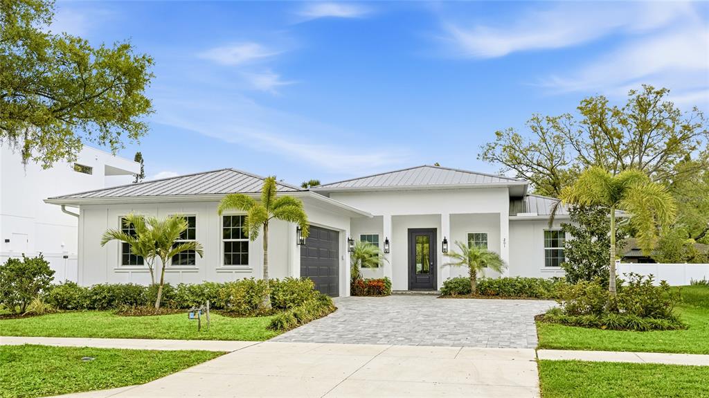A single-story white house with a metal roof, dark garage door, and a paved driveway — 201 S SHADE AVENUE, SARASOTA, FL