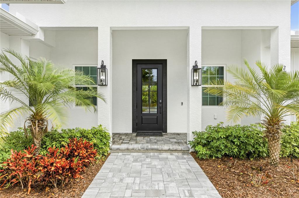 A paved walkway leads to the black front door of a white house with palm trees — 201 S SHADE AVENUE, SARASOTA, FL