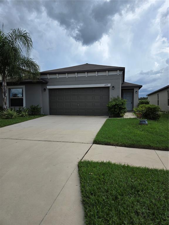 A gray single-story house features a two-car garage, a front entrance, and a palm tree — 1677 BLUE ROSE DRIVE, RUSKIN, FL