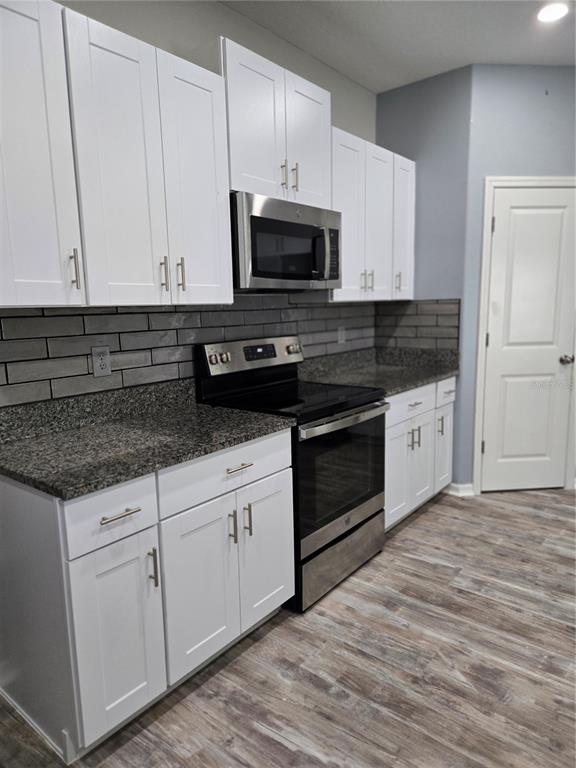 A kitchen features white cabinets, granite countertops, a gray subway tile backsplash, and stainless appliances — 1677 BLUE ROSE DRIVE, RUSKIN, FL