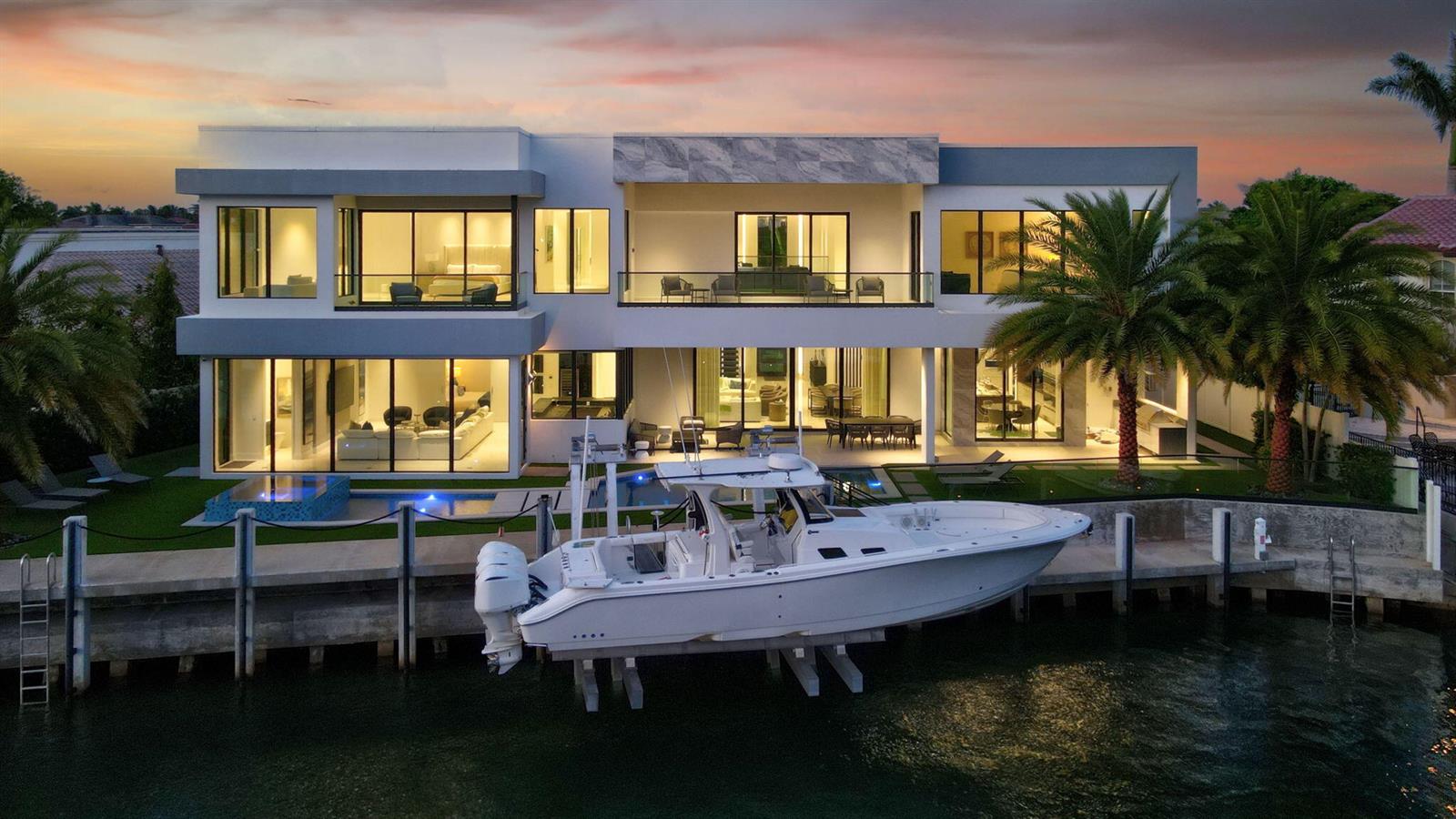 A modern two-story waterfront home with a boat docked at a private pier at dusk — 749 Bamboo Drive, Boca Raton FL 33432, BOCA RATON, FL