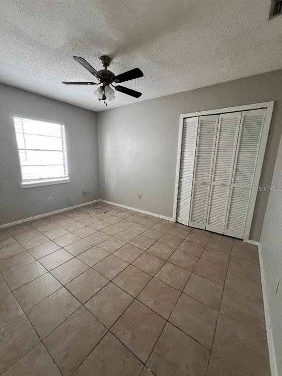 A bedroom with light gray walls, tile flooring, a ceiling fan, and white louvered closet doors — 267 LAKE THOMAS DRIVE, WINTER HAVEN, FL