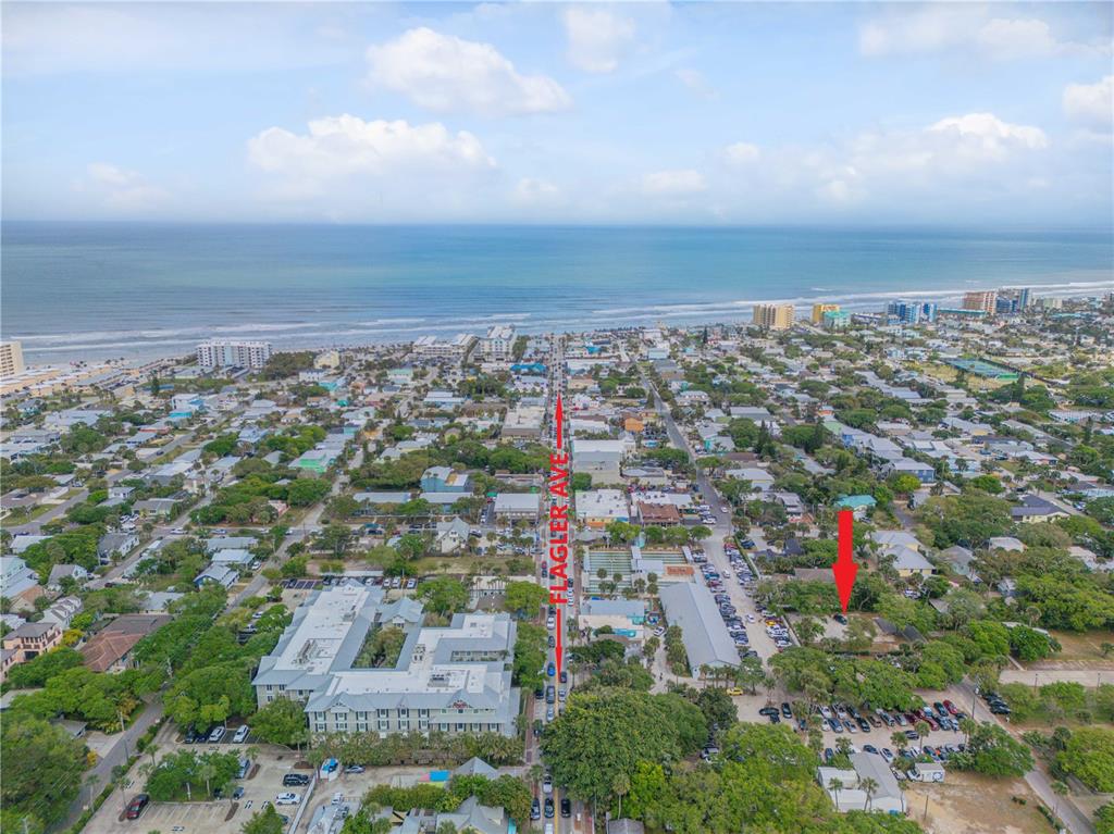 An aerial view shows a coastal town with a red arrow pointing toward a vacant lot — 214 COLUMBUS AVENUE, NEW SMYRNA BEACH, FL