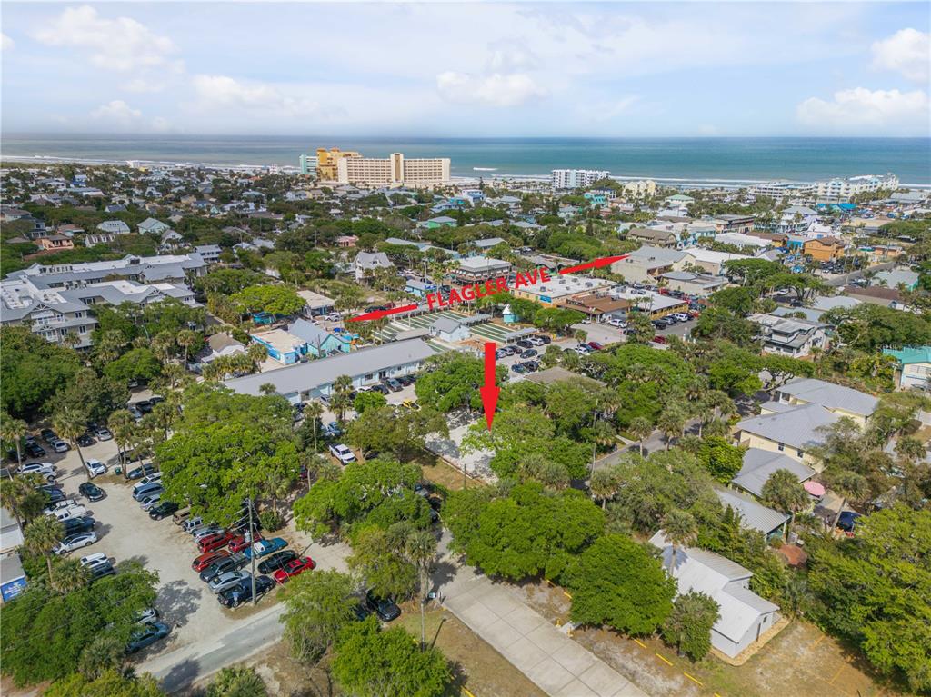 This aerial view shows a vacant lot surrounded by trees, parking areas, and nearby buildings — 214 COLUMBUS AVENUE, NEW SMYRNA BEACH, FL