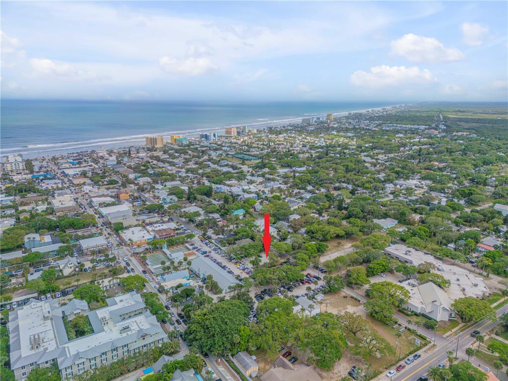 An aerial view shows a coastal town with a red arrow pointing to a specific property — 214 COLUMBUS AVENUE, NEW SMYRNA BEACH, FL