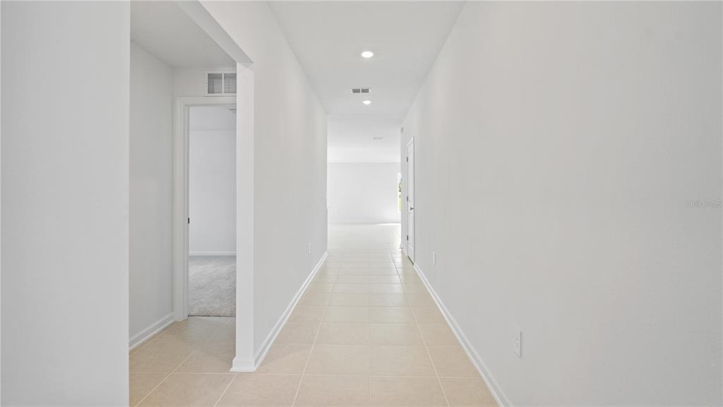 A long hallway with light-colored tile flooring leads to an open living area — 1952 PINE MEADOWS GOLFCOURSE ROAD, EUSTIS, FL