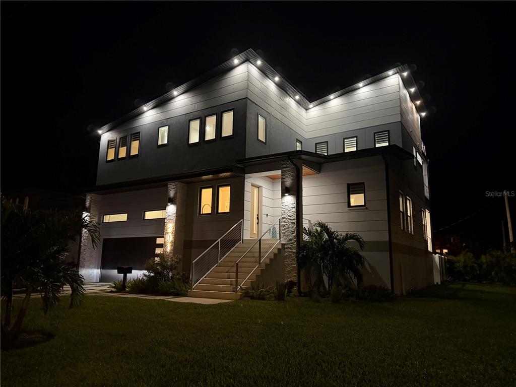 A modern two-story house with exterior lighting, stone accents, and a raised front staircase at night — 301 79TH STREET S, ST PETERSBURG, FL