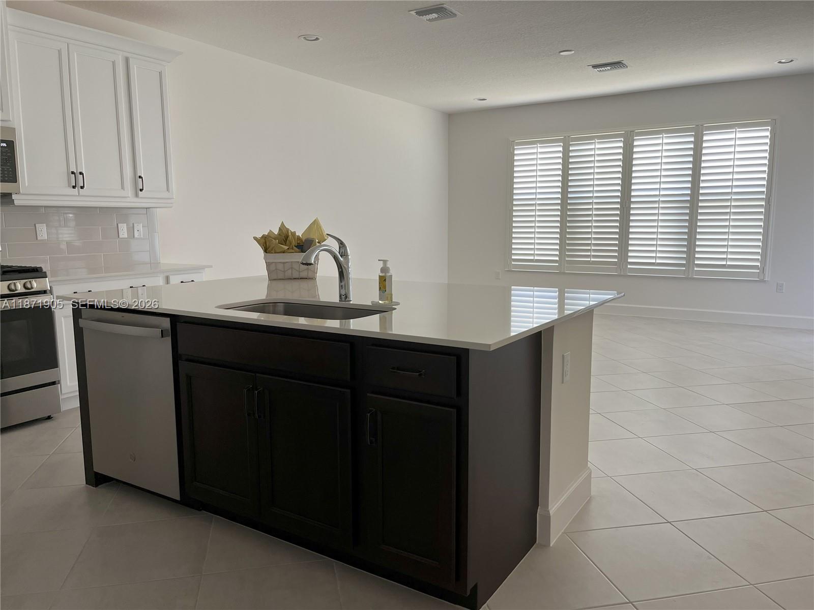 A kitchen island with a sink and dark cabinets sits in front of white kitchen cabinetry — PORT ST. LUCIE, FL