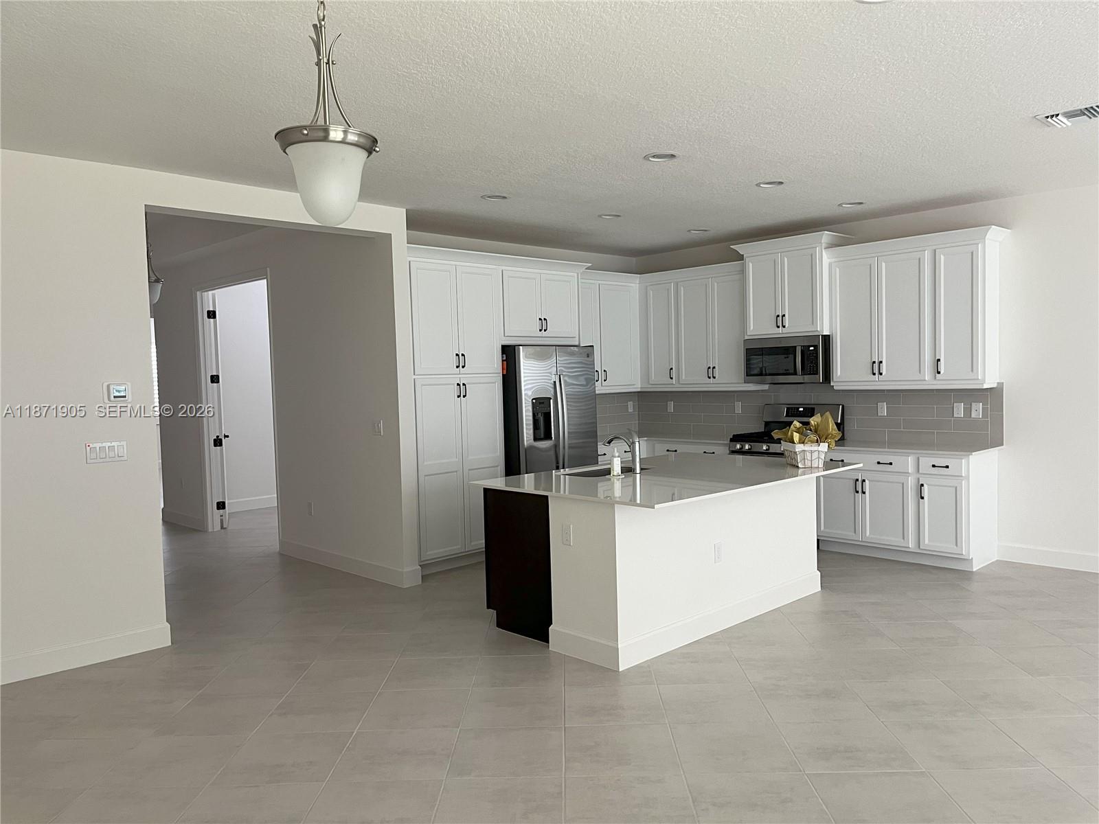 A modern kitchen features white cabinetry, a central island, and light gray tile flooring — PORT ST. LUCIE, FL