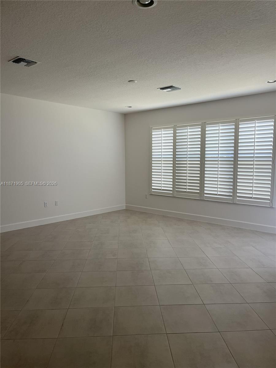 An empty room features light-colored tile flooring, white walls, and windows covered by plantation shutters — PORT ST. LUCIE, FL
