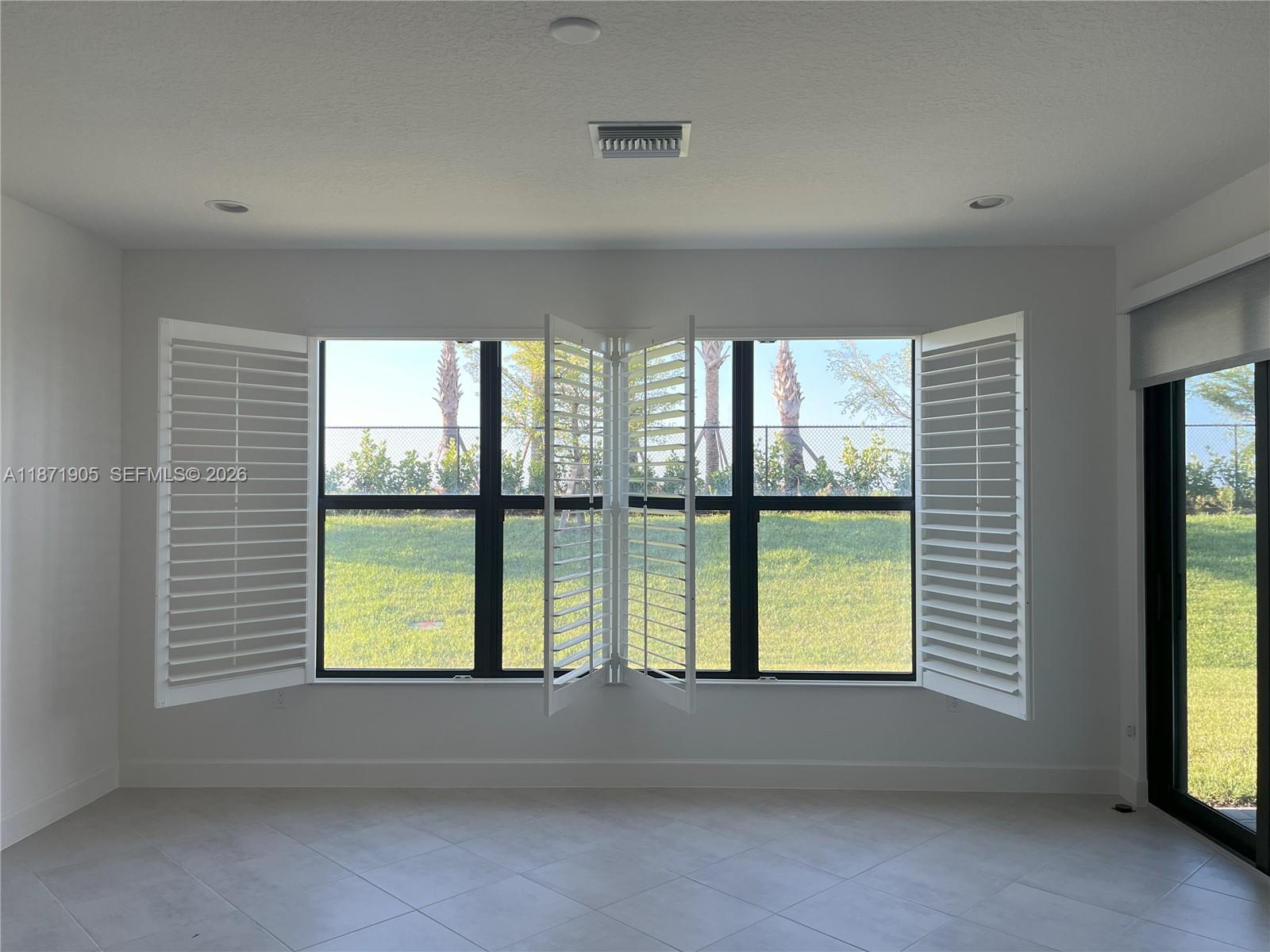 A bright room features white plantation shutters on a large window overlooking a grassy yard — PORT ST. LUCIE, FL