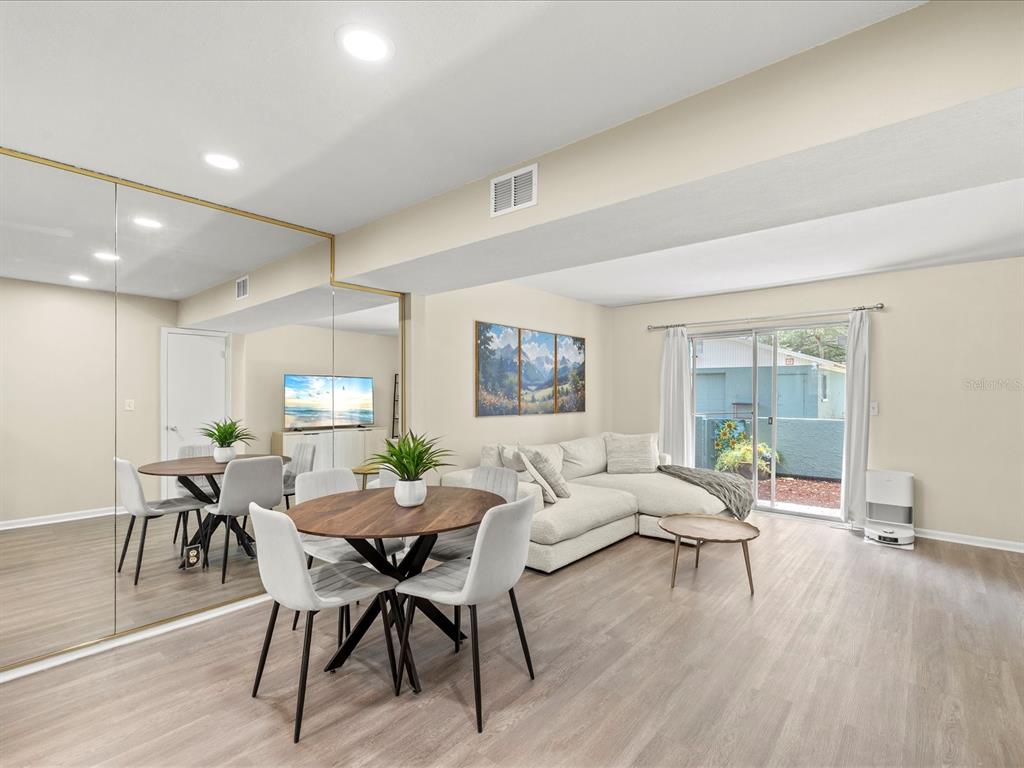 A living and dining area features light wood flooring, a sectional sofa, and mirrored walls — 179 114TH AVENUE N UNIT 179, ST PETERSBURG, FL