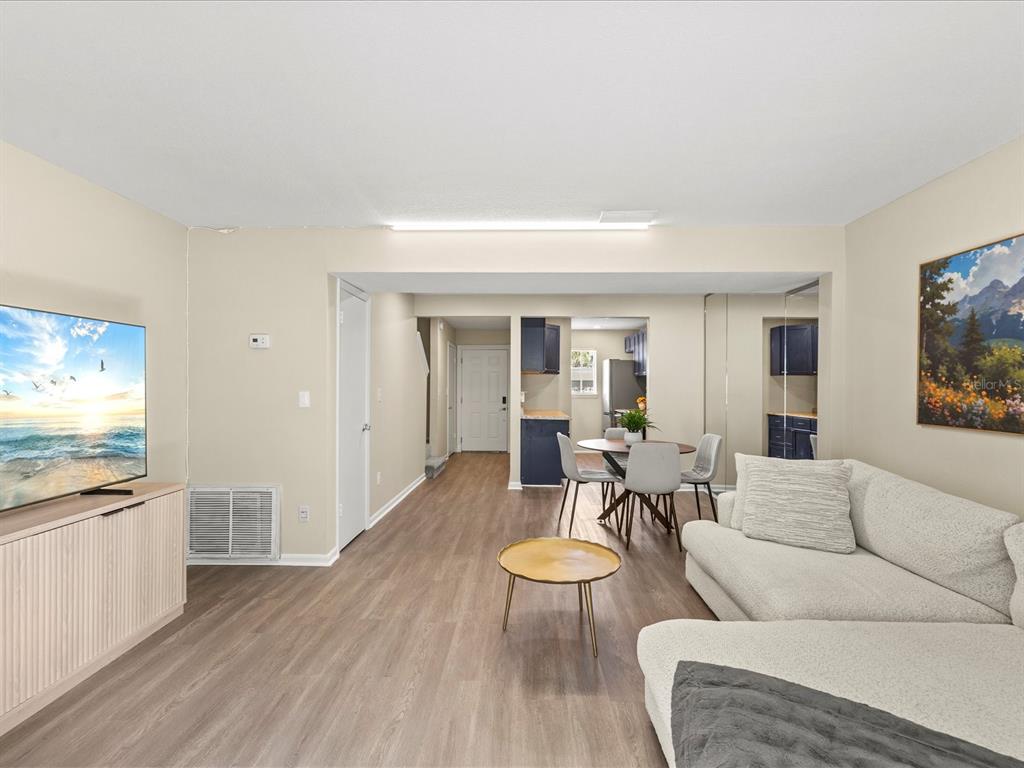 A living room with light wood-look flooring, a sectional sofa, and an adjacent dining area — 179 114TH AVENUE N UNIT 179, ST PETERSBURG, FL