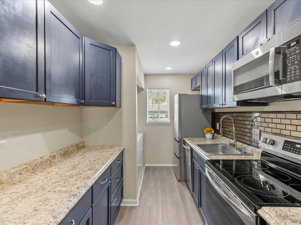 A galley kitchen features dark blue cabinets, granite countertops, stainless steel appliances, and a window — 179 114TH AVENUE N UNIT 179, ST PETERSBURG, FL
