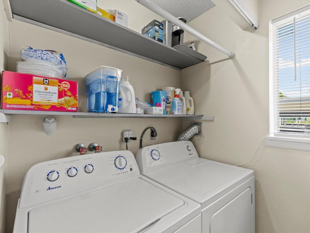 A laundry room features an Amana washer and dryer beneath two open storage shelves — 179 114TH AVENUE N UNIT 179, ST PETERSBURG, FL