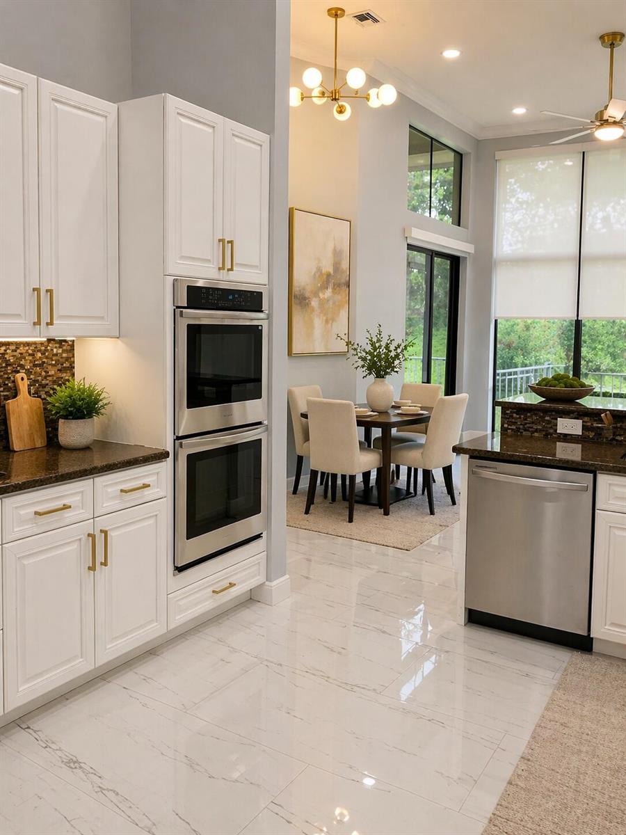 A kitchen with white cabinets, stainless steel appliances, and a dining area in the background — 10295 Trianon Place, Wellington FL 33449, WELLINGTON, FL