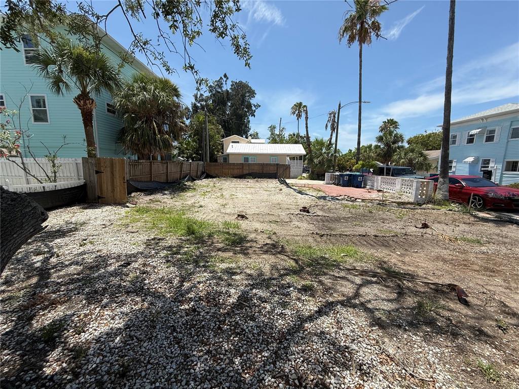 A vacant, sandy residential lot is situated between two light blue houses — 8586 E BAY DRIVE, TREASURE ISLAND, FL