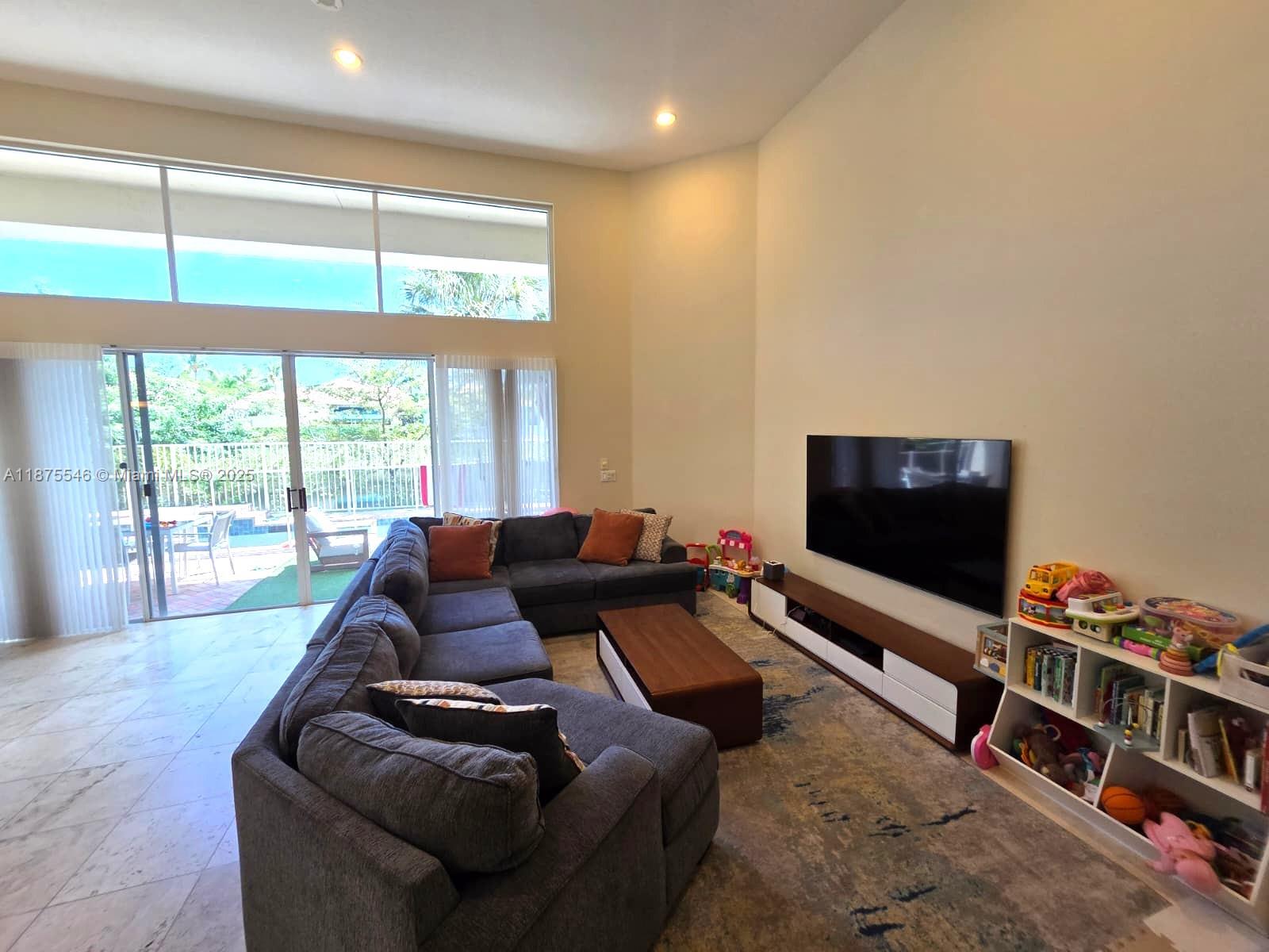 A living room features a large sectional sofa, a wall-mounted television, and floor-to-ceiling windows — 7030 Islegrove Pl, Boca Raton FL 33433, BOCA RATON, FL