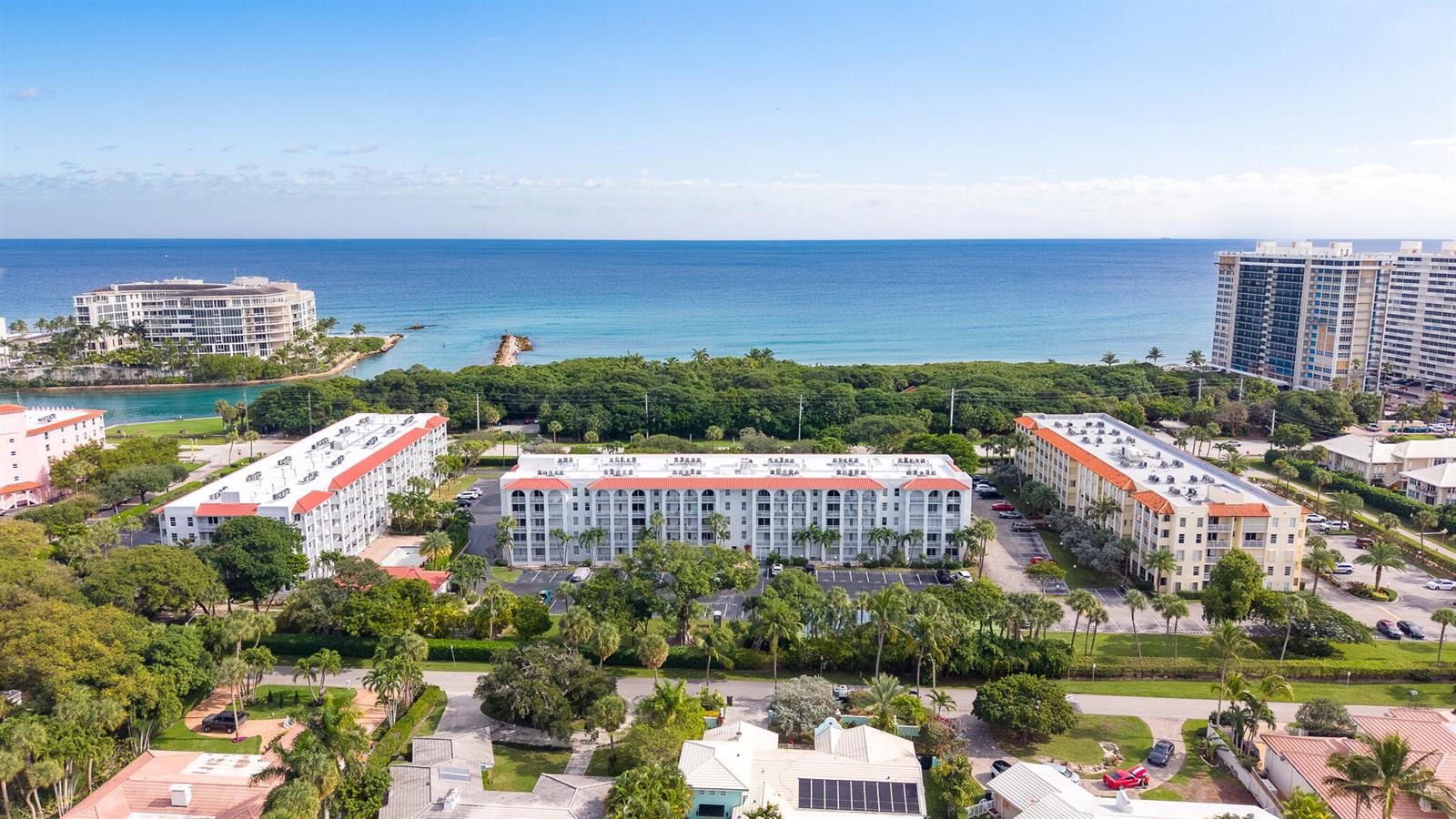 An aerial view shows several multi-story apartment buildings surrounded by lush trees near the ocean — 950 Ponce De Leon Road # 209, Boca Raton FL 33432, BOCA RATON, FL