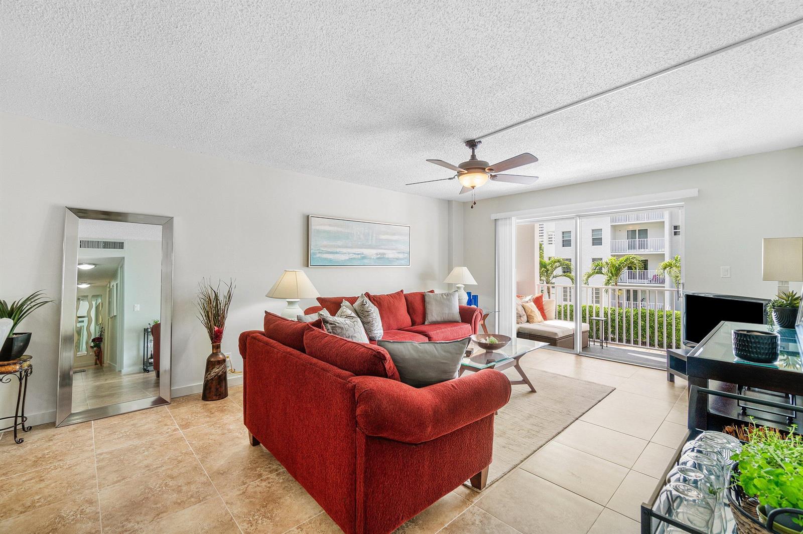 A living room features a red sofa, tile flooring, a ceiling fan, and a balcony — 950 Ponce De Leon Road # 209, Boca Raton FL 33432, BOCA RATON, FL