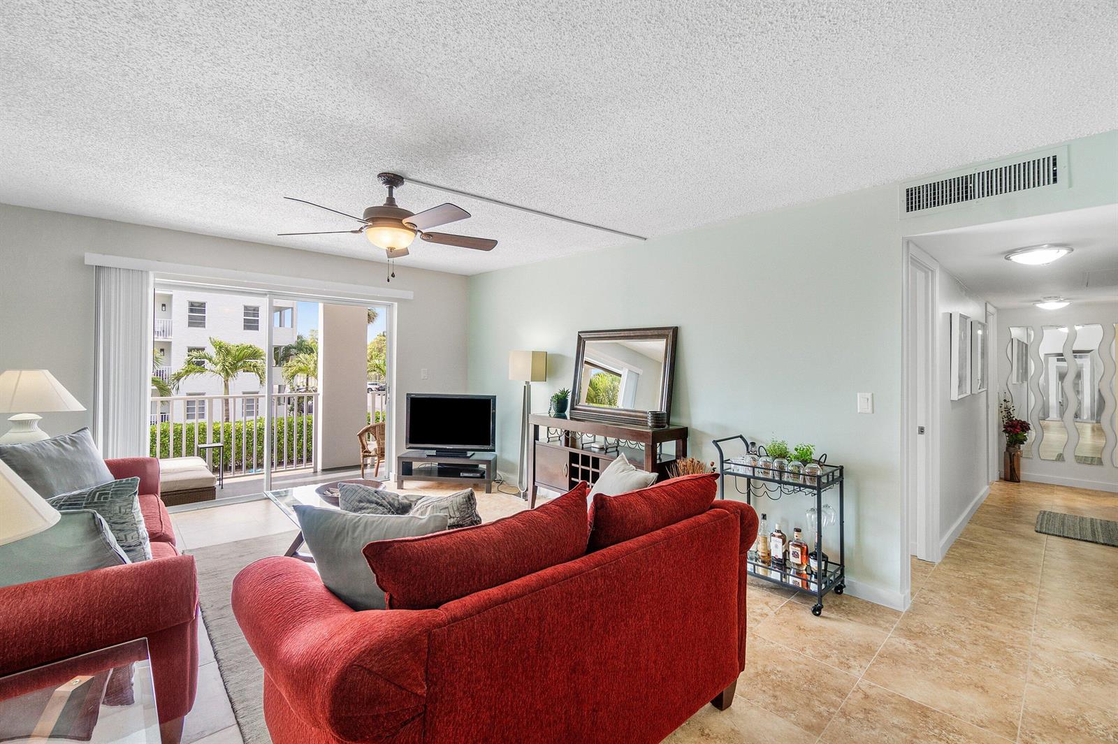A living room features red sofas, a ceiling fan, a bar cart, and a balcony — 950 Ponce De Leon Road # 209, Boca Raton FL 33432, BOCA RATON, FL