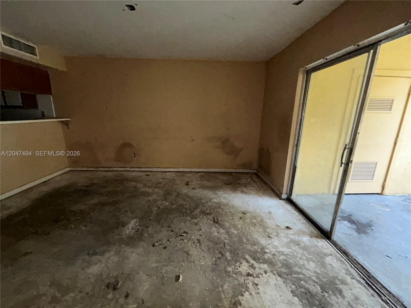 An empty room features stained walls, a concrete floor, and a sliding glass door — 15340 SW 106th Ter # 817, Miami FL 33196, MIAMI, FL