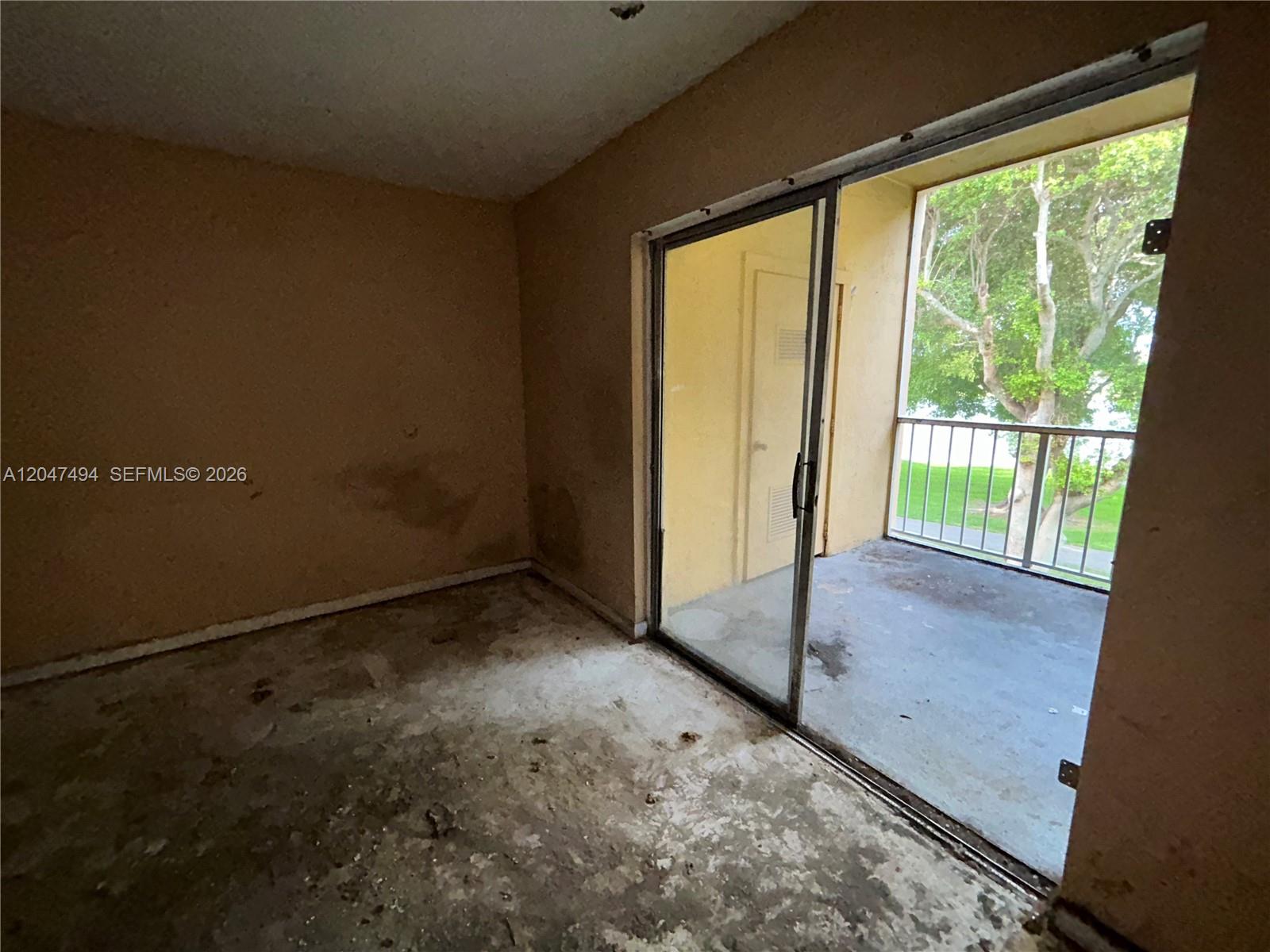 An empty room with stained walls and concrete flooring leads to a balcony with railings — 15340 SW 106th Ter # 817, Miami FL 33196, MIAMI, FL
