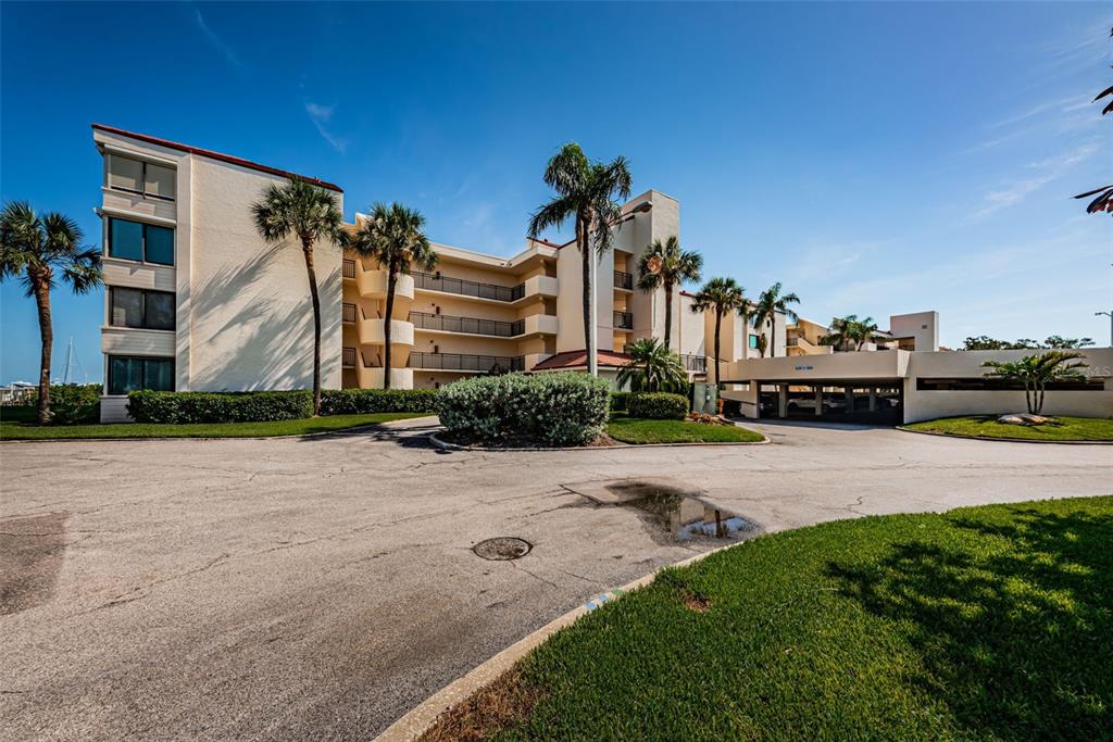 A multi-story apartment building with balconies and palm trees sits behind a paved driveway — 5825 PUERTA DEL SOL BOULEVARD S UNIT 166, ST PETERSBURG, FL