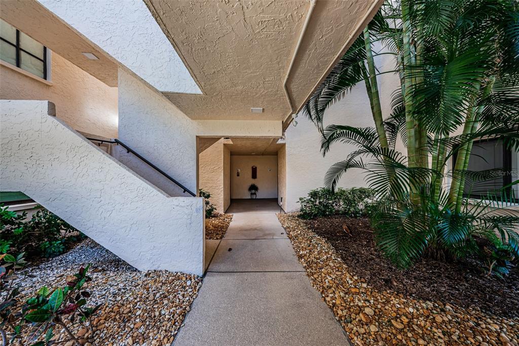 A concrete walkway leads to an entryway beneath a covered outdoor staircase and palm trees — 5825 PUERTA DEL SOL BOULEVARD S UNIT 166, ST PETERSBURG, FL