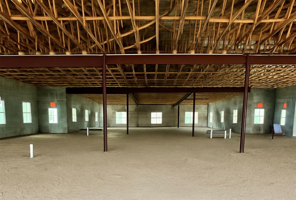 An unfinished interior space features concrete walls, exposed wooden ceiling trusses, and steel support beams — 981 VINELAND ROAD, WINTER GARDEN, FL