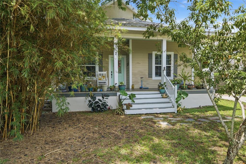 A tan bungalow with a front porch, white stairs, and lush landscaping in the yard — 512 SE 9TH STREET, OCALA, FL