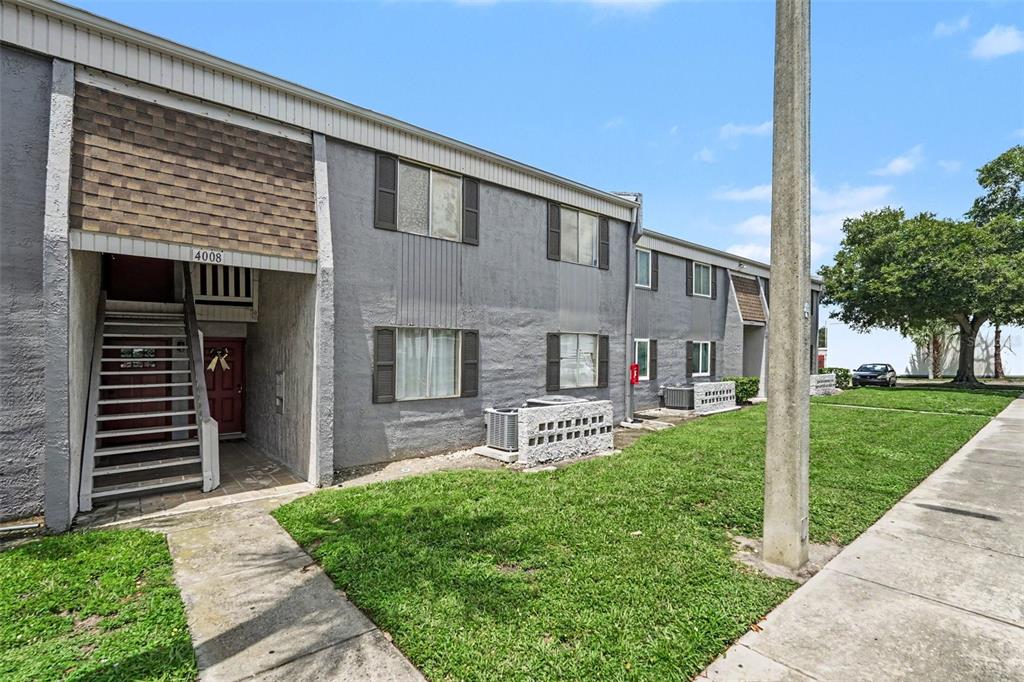 A two-story gray apartment building features an exterior staircase and a grassy front lawn — 4008 CORTEZ DRIVE UNIT B, TAMPA, FL
