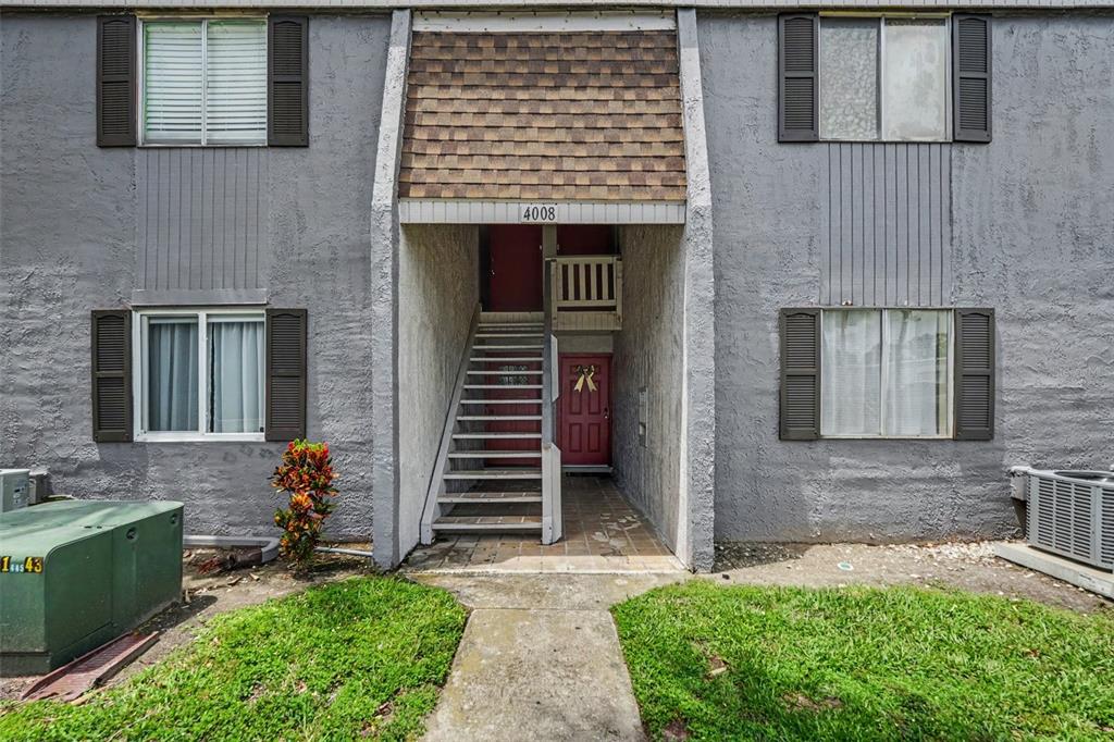 Exterior view of a two-story apartment building with gray stucco walls and red doors — 4008 CORTEZ DRIVE UNIT B, TAMPA, FL